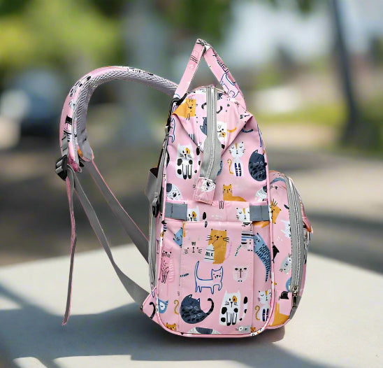 Voici le Sac pour Bebe | Chat : un sac à dos rose avec une seule bretelle grise, de multiples compartiments zippés et une organisation intelligente. Son tissu est orné de chats de dessins animés dans diverses poses pour plus de charme et de polyvalence.