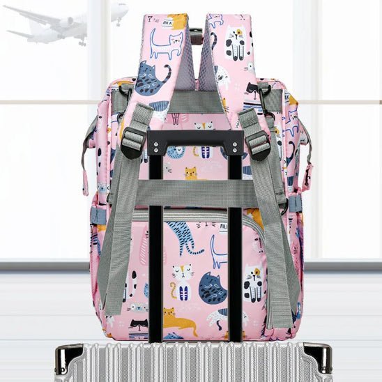 Un Sac pour Bébé | Chat, comportant des illustrations colorées de chats et un système d'organisation intelligent, est attaché à une poignée de valise argentée, tandis qu'un avion vole à l'extérieur des grandes fenêtres en arrière-plan.