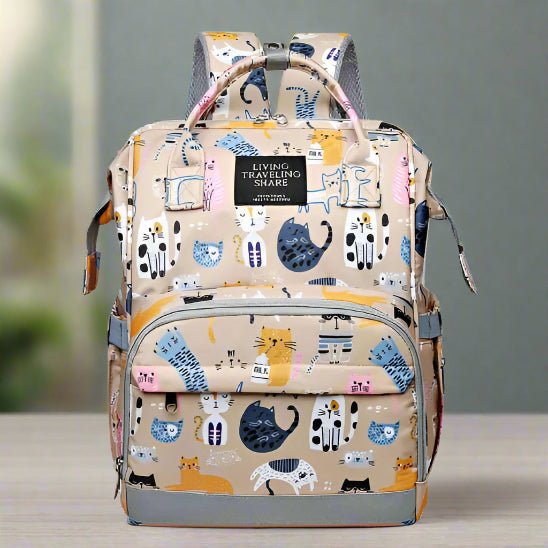 Le Sac pour Bebe | DesignChat est un sac à dos beige multifonction pour bébé avec des motifs de chats colorés. Il est doté d'une poche frontale, d'une poignée supérieure, de bretelles réglables et d'une étiquette "Living Traveling Share".