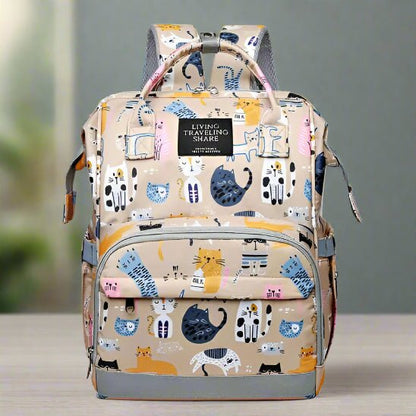 Le Sac pour Bebe | DesignChat est un sac à dos beige multifonction pour bébé avec des motifs de chats colorés. Il est doté d'une poche frontale, d'une poignée supérieure, de bretelles réglables et d'une étiquette "Living Traveling Share".