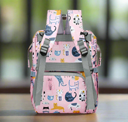 Le Sac pour Bebe | Chat est un sac à dos rose avec des bretelles et des fermetures éclair grises, avec un motif de chat ludique dans différentes couleurs et poses. Ce sac polyvalent comprend plusieurs poches, des bretelles réglables et un système d'organisation intelligent pour tous vos essentiels.