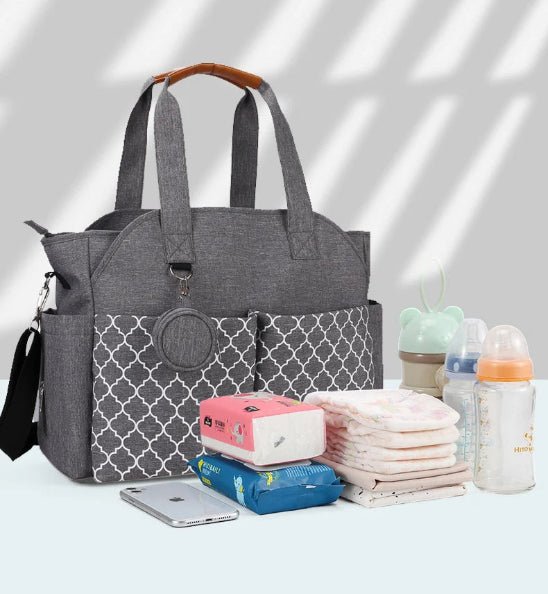 Un Sac pour Maternité - LeComplet pour bébé gris avec des poches frontales à motifs est placé à côté d'articles essentiels pour bébé - des lingettes humides, des couches, des biberons, un étui à sucette et un smartphone - disposés de manière ordonnée sur une surface claire.