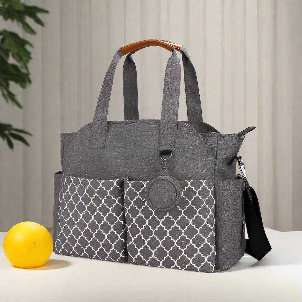 Le Sac pour Maternité est un sac fourre-tout gris avec des poches avant géométriques, des poignées décoratives marron, un porte-clés rond, une bandoulière noire réglable et une grande capacité - polyvalent et parfait pour un usage quotidien.