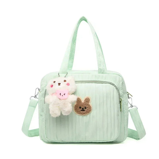 Le Sac pour la maternité | Longchamp est un sac à langer vert clair doté d'une poche zippée sur le devant, d'un porte-clés en peluche ours et d'un patch lapin marron brodé. Idéal pour les parents nomades, il est doté de deux anses et d'une bandoulière réglable.