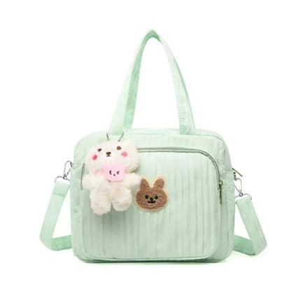 Le Sac pour la maternité | Longchamp est un sac à langer vert clair doté d'une poche zippée sur le devant, d'un porte-clés en peluche ours et d'un patch lapin marron brodé. Idéal pour les parents nomades, il est doté de deux anses et d'une bandoulière réglable.